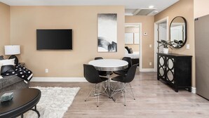 A modern living room with a round dining table, black chairs, a sofa, a flat-screen TV, and a large abstract painting.