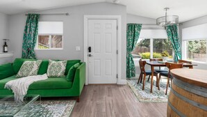 Ein Zimmer mit einem grünen Sofa, einem Esstisch mit Stühlen, einem Holzbottich und einer weißen Tür.