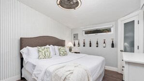 Ein ordentlich eingerichtetes Schlafzimmer mit Bett, Nachttisch, Lampe und einer Wandweineinrichtung.