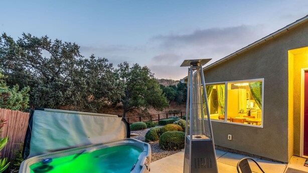 Ein moderner Outdoor-Whirlpool mit Metallrahmen, einer Holzterrasse und Blick auf ein Haus mit einem großen Fenster.
