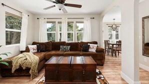 A living room with a brown sofa, a wooden chest, a ceiling fan, and large windows. - 2Bed 2 Bath Cottage onMicro Resort near Downtown (Paso Robles)