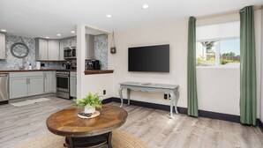 Een moderne keuken met inbouwapparatuur, een eethoek met een ronde tafel, en een flatscreen televisie aan de muur.