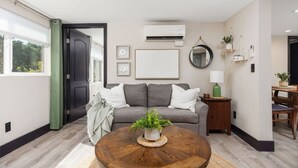 Een moderne woonkamer met een grijze bank, een ronde houten salontafel en een potplant.