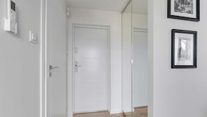 A hallway with a white door, a thermostat, and framed pictures on the wall. - Petit Repit by Grand Apartments (Sopot)