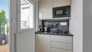 A compact kitchen with white cabinets, a black countertop, a microwave, and a window overlooking a balcony. - Petit Repit by Grand Apartments (Sopot)