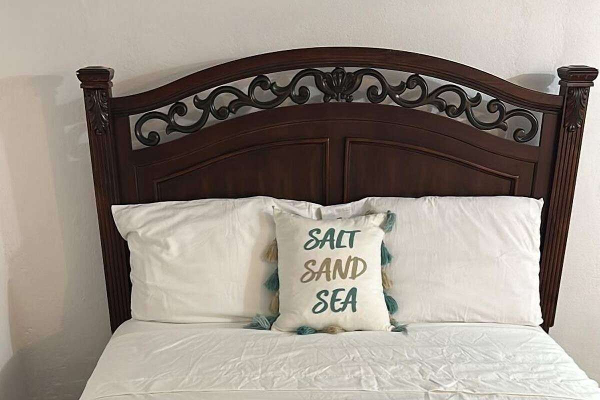 Ein Bett mit weißer Bettdecke und zwei Kissen, eines mit dem Aufdruck "SALT, SAND, SEA".
