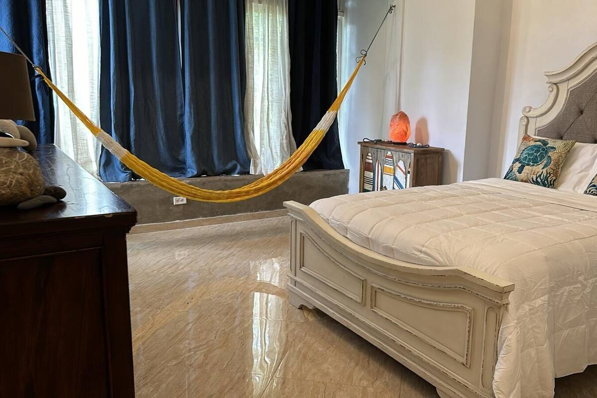 Ein Schlafzimmer mit einem Bett, einem Nachttisch, einer Lampe und einer Hängematte.