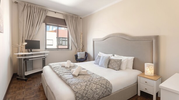 A neatly arranged bedroom with a bed, bedside table, and a desk with a computer.
