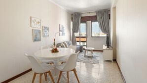 A dining area with a round table and chairs, a sofa, and a window with curtains.