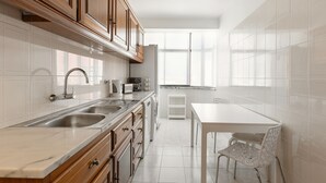 A modern kitchen with wooden cabinets, a double sink, a white countertop, and a dining area with a table and chairs.