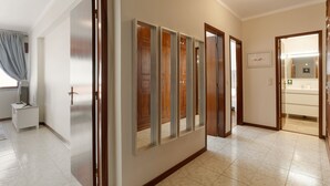 A hallway with a wooden wardrobe, a white bedside table, and a bathroom visible through a glass door.