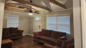 Un salon avec des poutres en bois, un ventilateur de plafond, deux canapés marron et une porte avec une fenêtre.