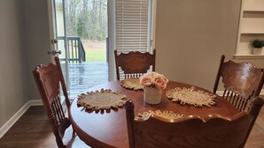 Une table à manger avec quatre chaises, un vase rempli de fleurs et, à travers une porte vitrée, une vue sur une terrasse et des arbres.