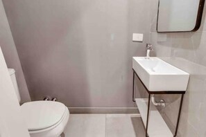 A modern bathroom with a white toilet, a white sink with a wooden base, and a mirror above the sink.