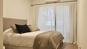 Een slaapkamer met een bed, witte gordijnen en een airconditioner.