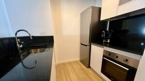 Een kleine keuken met een zwart aanrecht, roestvrijstalen apparatuur en een houten vloer.