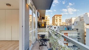Varanda com mesa, cadeiras, um vaso de planta e vista dos edifícios ao redor.