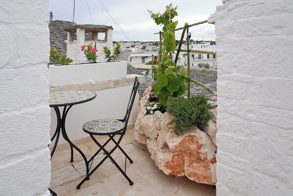 A small outdoor patio with a round table and a chair, a climbing plant, and a white wall. - TrulliOcchiDiPietraHistoricalExperience (Alberobello)