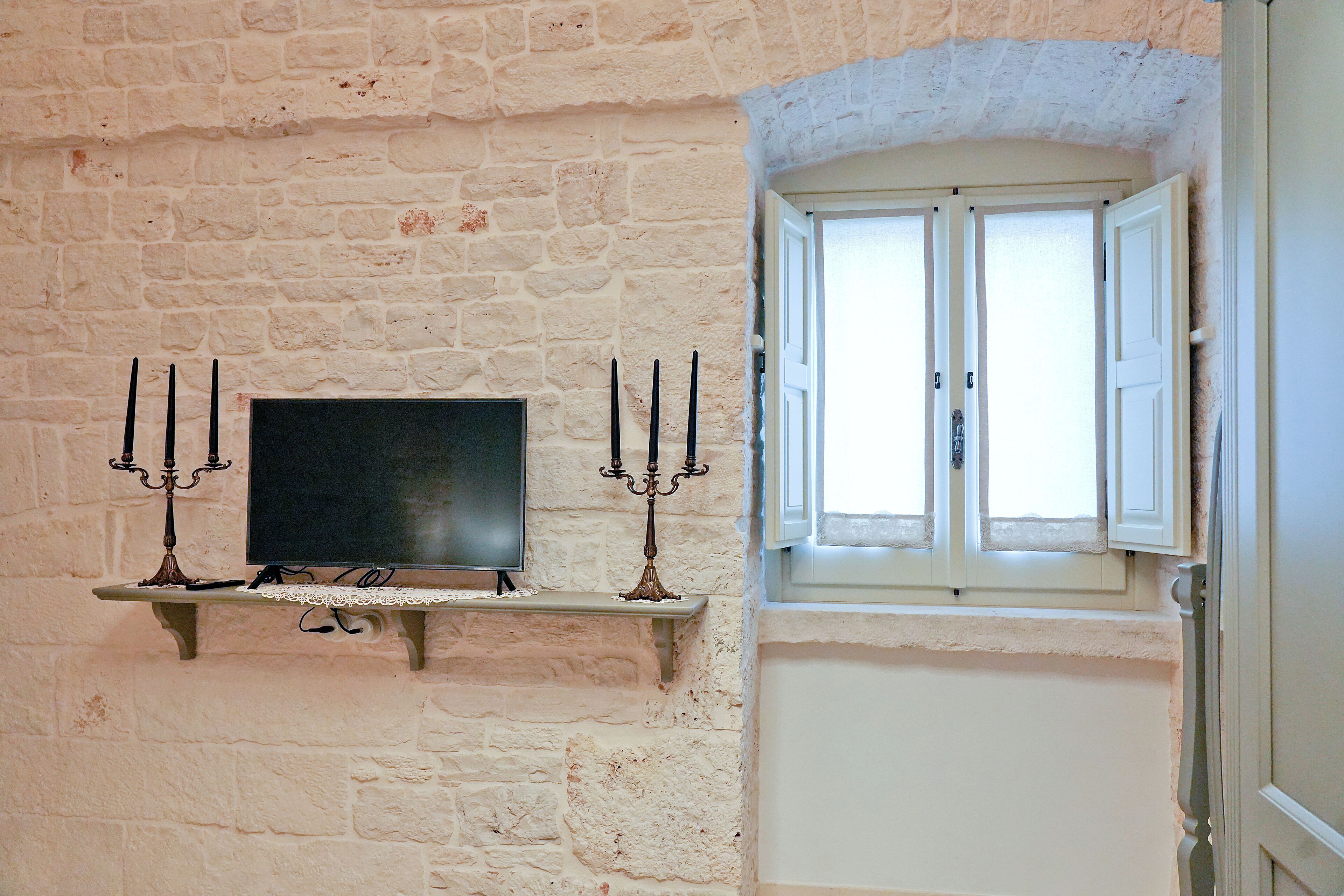 Ein Zimmer mit einer Steinwand, einem kleinen Regal mit Fernseher und einem Fenster mit weißen Fensterläden.