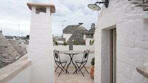 A small outdoor patio with a white wall, a stone chimney, and a table with two chairs. - TrulliOcchiDiPietraHistoricalExperience (Alberobello)