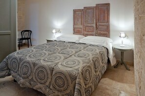 A bedroom with a large bed, two bedside tables with lamps, a chair, and a wooden door. - TrulliOcchiDiPietraHistoricalExperience (Alberobello)