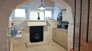 A kitchen with a stone archway, a fireplace, and a hanging light fixture. - TrulliOcchiDiPietraHistoricalExperience (Alberobello)