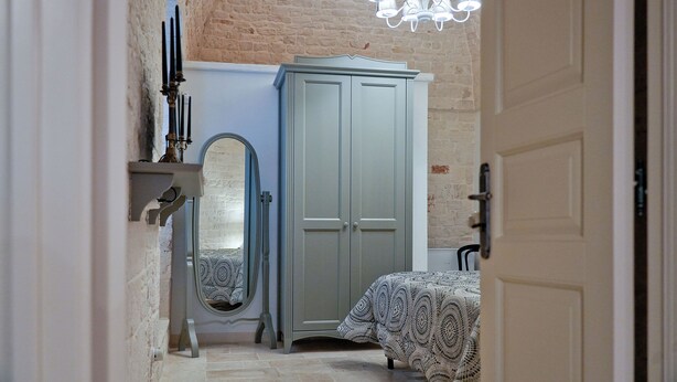 A bedroom with a bed, a wardrobe, a mirror, and a chandelier. - TrulliOcchiDiPietraHistoricalExperience (Alberobello)