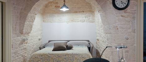 A room with a bed, a clock, and a table with a glass.
