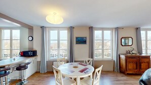 Un espace repas comprenant une table ronde, des chaises, un bar avec des tabourets, un buffet en bois et une vue dégagée grâce à de grandes fenêtres.