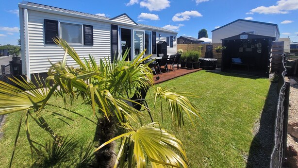 A mobile home with a patio, a small garden, and a neighboring house. - Chalet Sea-renity Lakeside met Jacuzzi (Jabekke)