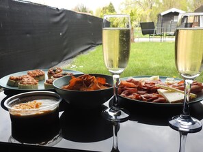 A table with food and drinks, including a bowl of chips, a plate of meats, and two glasses of white wine.