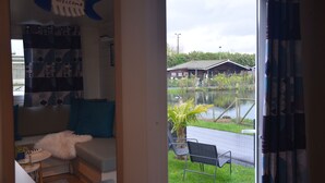 A room with a sofa, a small table with a plant, and a view of a building and water outside. - Chalet Sea-renity Lakeside met Jacuzzi (Jabekke)