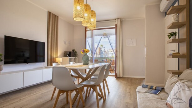 Ein modernes Wohnzimmer mit einer Couch, einem Essbereich mit Stühlen und Tisch, einem an der Wand befestigten Fernseher und einem großen Fenster mit Blick.