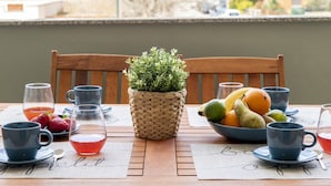 Ein gedeckter Tisch mit blauen Tassen, einer Obstschale und einem Korbwesen mit Grünpflanzen.