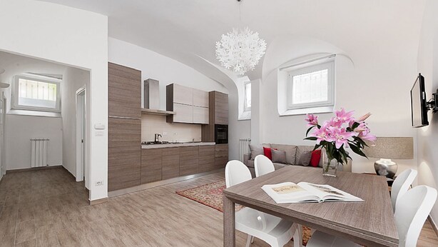 Een moderne keuken met een centraal eiland, een eethoek met een tafel en stoelen, en een woongedeelte met een bank en een decoratieve vaas.