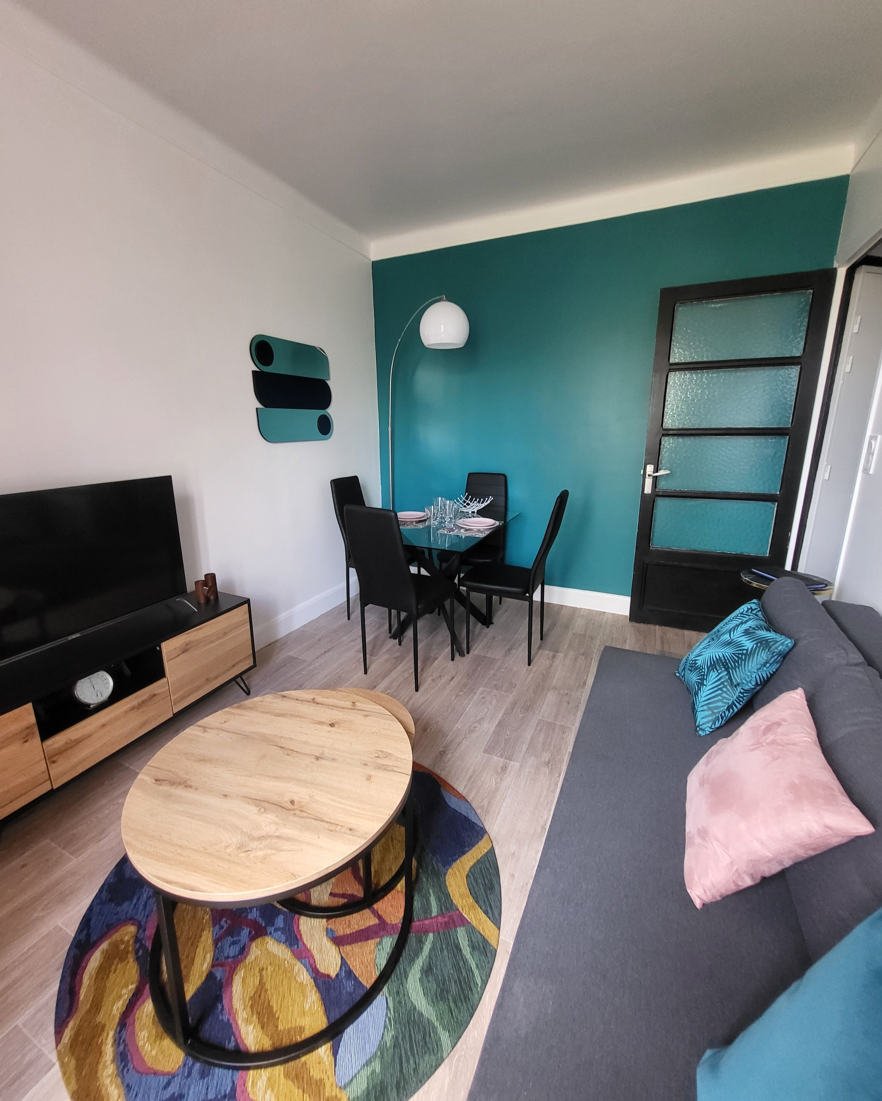 A modern living room with a sofa, a coffee table, a TV, and a dining area with chairs and a table.