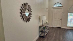 A hallway with a wooden wall art piece, a table with a lamp, and a door with a window above it. - FIFA 2026‼️ Modern 3 bedroom home for stay! AT&T Stadium, Globe Life Field. (Mansfield)