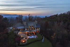 A large house with a pool and outdoor lighting, surrounded by trees and a view of the mountains. - Heated Pool/Hot Tub/Theatre/Game/Fire/Sleep 34 (Gatlinburg)