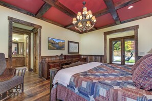Ein Schlafzimmer mit einem großen Bett, Holzmöbeln, einer Kandelaber und Blick durch eine Glastür.
