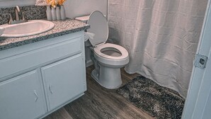 Ein Badezimmer mit Toilette, einem Waschbecken mit Granitplatte, einem Spiegel und einem motivierenden Zitat an der Wand.