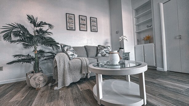 Ein Wohnzimmer mit einer Couch, einem runden Tisch, einer Topfpflanze und drei Wandbildern mit motivierenden Sprüchen.