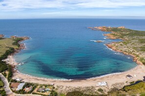 Vista aérea de una zona costera con una gran bahía, playa de arena y afloramientos rocosos.