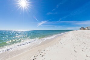 A beach with a clear sky, a bright sun, and a calm sea. - 5BR Beach House+Steps To Beach+Balcony Gulf Views+Firepit+Elevator+Dog Friendly (Gulf Shores)