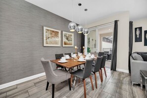 Un espace de salle à manger moderne avec une table en bois prévue pour quatre personnes, des chaises à revêtement gris et des luminaires suspendus.