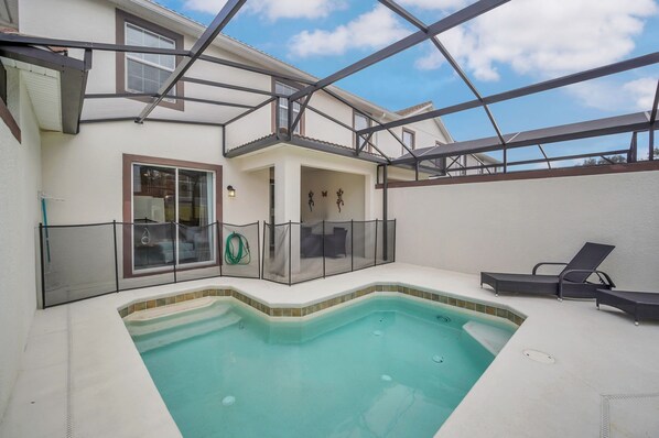 Une piscine dotée d’un patio couvert, d’une porte vitrée et d’un petit espace clos comprenant une chaise et une lampe.