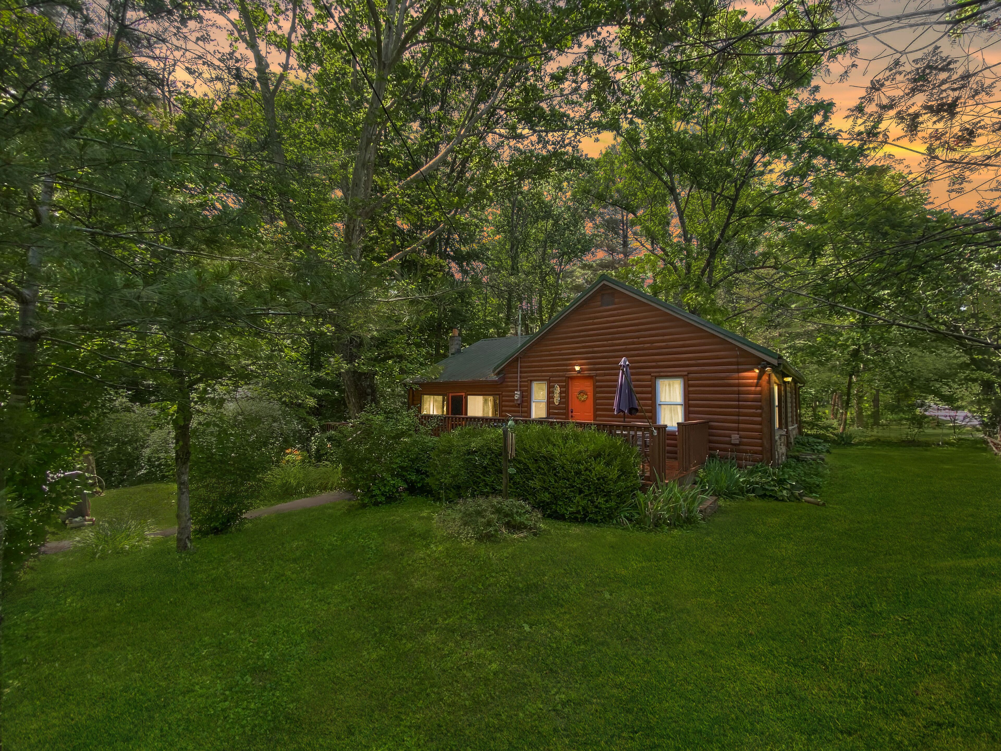 A wooden cabin with a porch, surrounded by lush greenery and trees.