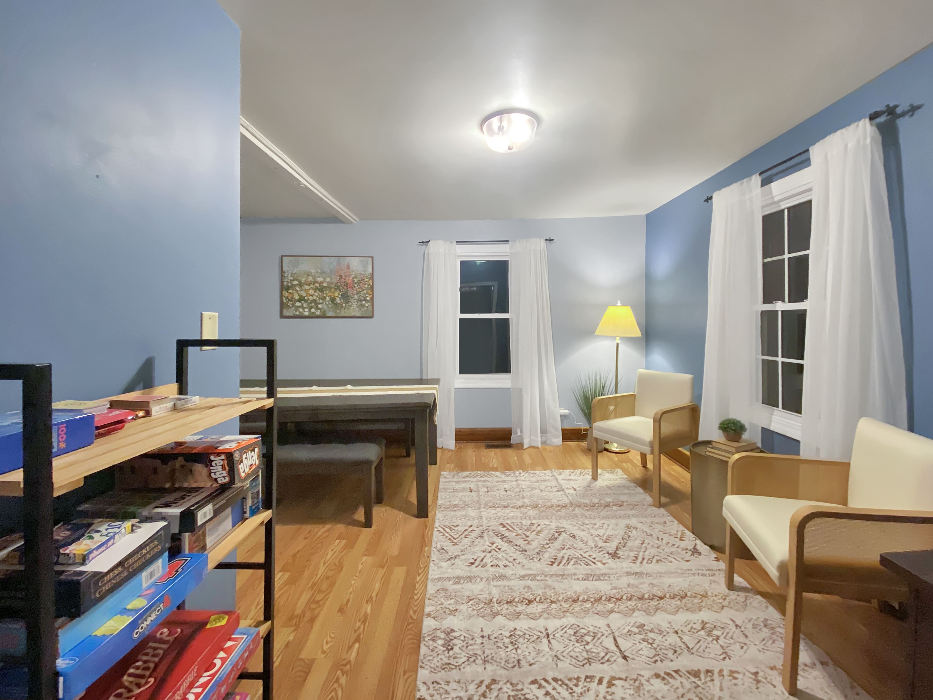 Une pièce avec un plancher en bois, un bureau, une chaise, une lampe et une bibliothèque contenant des jeux de société.
