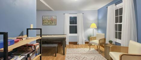 Une pièce avec un plancher en bois, un bureau, une chaise, une lampe et une bibliothèque contenant des jeux de société.