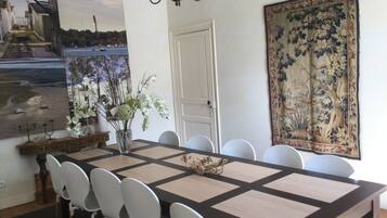 Un comedor con una mesa larga, sillas blancas, un jarrón con flores y dos cuadros grandes en las paredes.