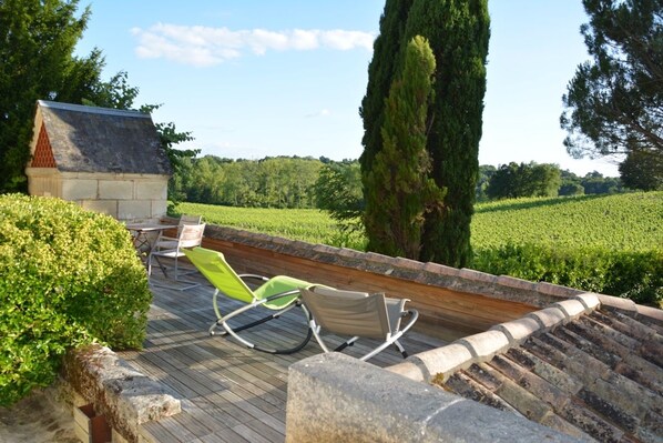 A wooden deck with two lounge chairs, a stone wall, and a small building with a sloped roof.